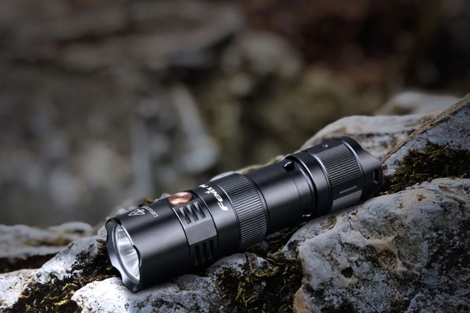 Na zdjęciu znajduje się latarka Fenix PD25R na skalistym tle.