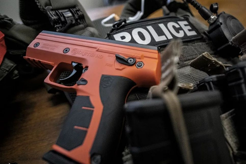 Zdjęcie przedstawia pomarańczowy pistolet na kule gumowe, kt&oacute;ry ułożony jest na policyjnej kamizelce.