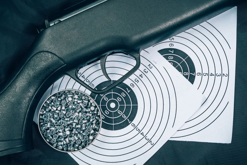 Zdjęcie przedstawia czarną wiatr&oacute;wkę ułożoną na papierowej tarczy strzeleckiej w towarzystwie śrut&oacute;w. 