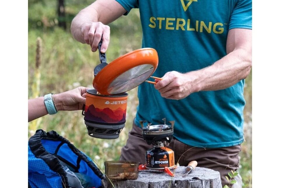 Mężczyzna przygotowujący posiłek na kuchence turystycznej Jetboil MiniMo w plenerze.